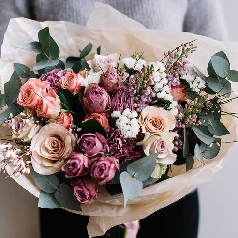 Junge Floristin, die frisch zubereiteten blühenden Blumenstrauß aus Rosen und Eukalyptus auf dem grauen Wandhintergrund hält.